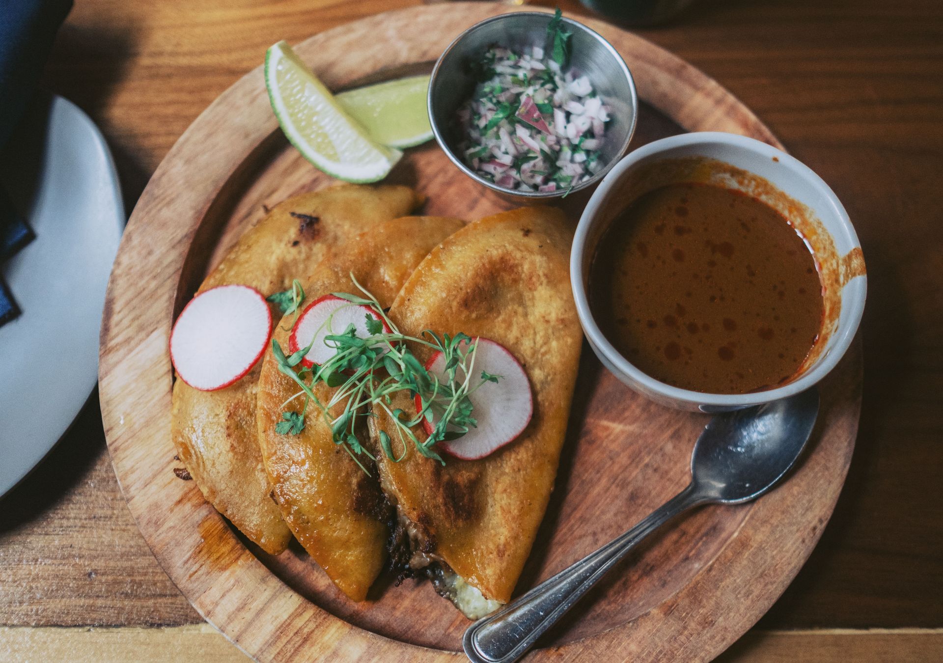 Close-up of traditional Mexican tacos served with radish, lime, and salsa on a wooden plate.